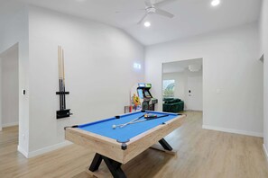 Une table de billard recouverte d’un drap bleu, un ventilateur de plafond et un porte-billes contenant les billes.