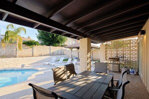 Un espace extérieur abrité comprenant une piscine, des chaises longues, un barbecue et une table avec des chaises.