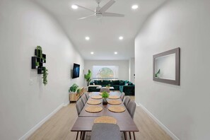 Un salon moderne comprenant un coin repas, un ventilateur de plafond et une grande fenêtre équipée de stores.