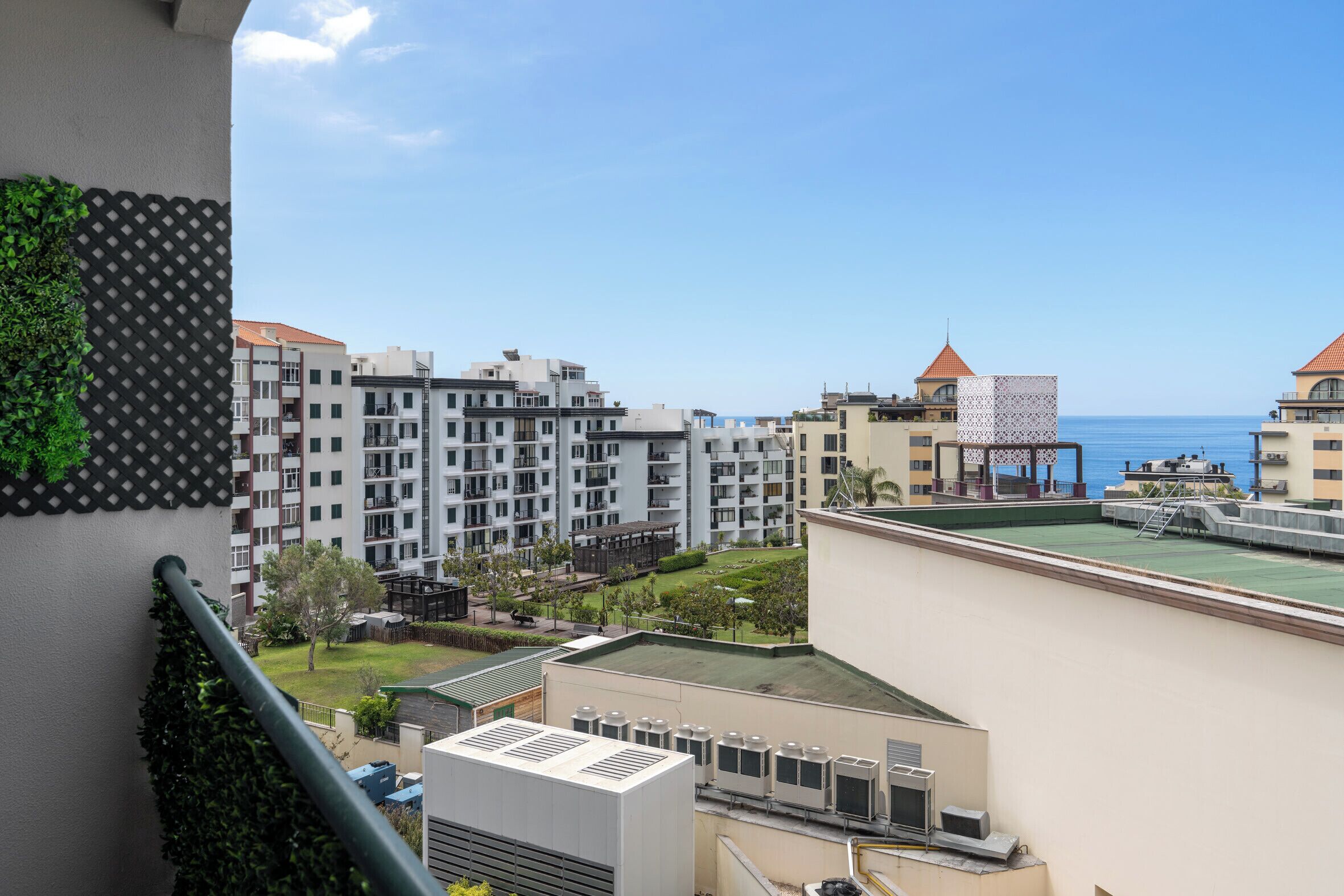 Un quartier résidentiel comprenant plusieurs immeubles d’appartements, une terrasse sur le toit avec des unités de climatisation, et une vue sur la mer.