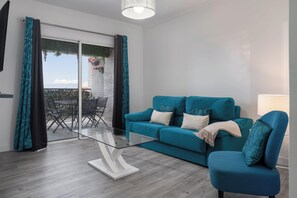 A modern living room with a teal sofa, a glass coffee table, and a blue armchair. - Ajuda VI – Comfortable Apartment in Funchal (Funchal)