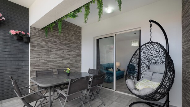 A modern outdoor dining area with a glass table and metal chairs, a hanging chair, and a sliding glass door leading to a living space. - Ajuda VI – Comfortable Apartment in Funchal (Funchal)