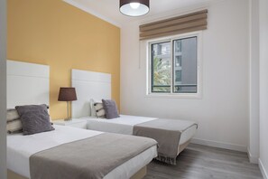 Ein Hotelzimmer mit zwei Betten, einem Fenster mit Jalousien, einer Lampe und Blick auf ein Gebäude.