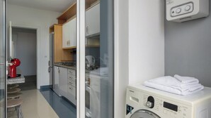A laundry room with a front-loading washing machine, a red coffee machine, and a kitchen area with cabinets and a countertop. - Ajuda VI – Comfortable Apartment in Funchal (Funchal)
