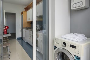 Ein Waschraum mit einer Frontlader-Waschmaschine, einer roten Kaffeemaschine und einer Küchenzeile inklusive Schränken und Arbeitsplatte.