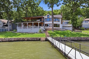 A two-story house with a covered porch and a stone staircase leading to the upper level. - A Stunning east facing, lake front home, in a cove, with Main Channel Views! (Sunrise Beach)
