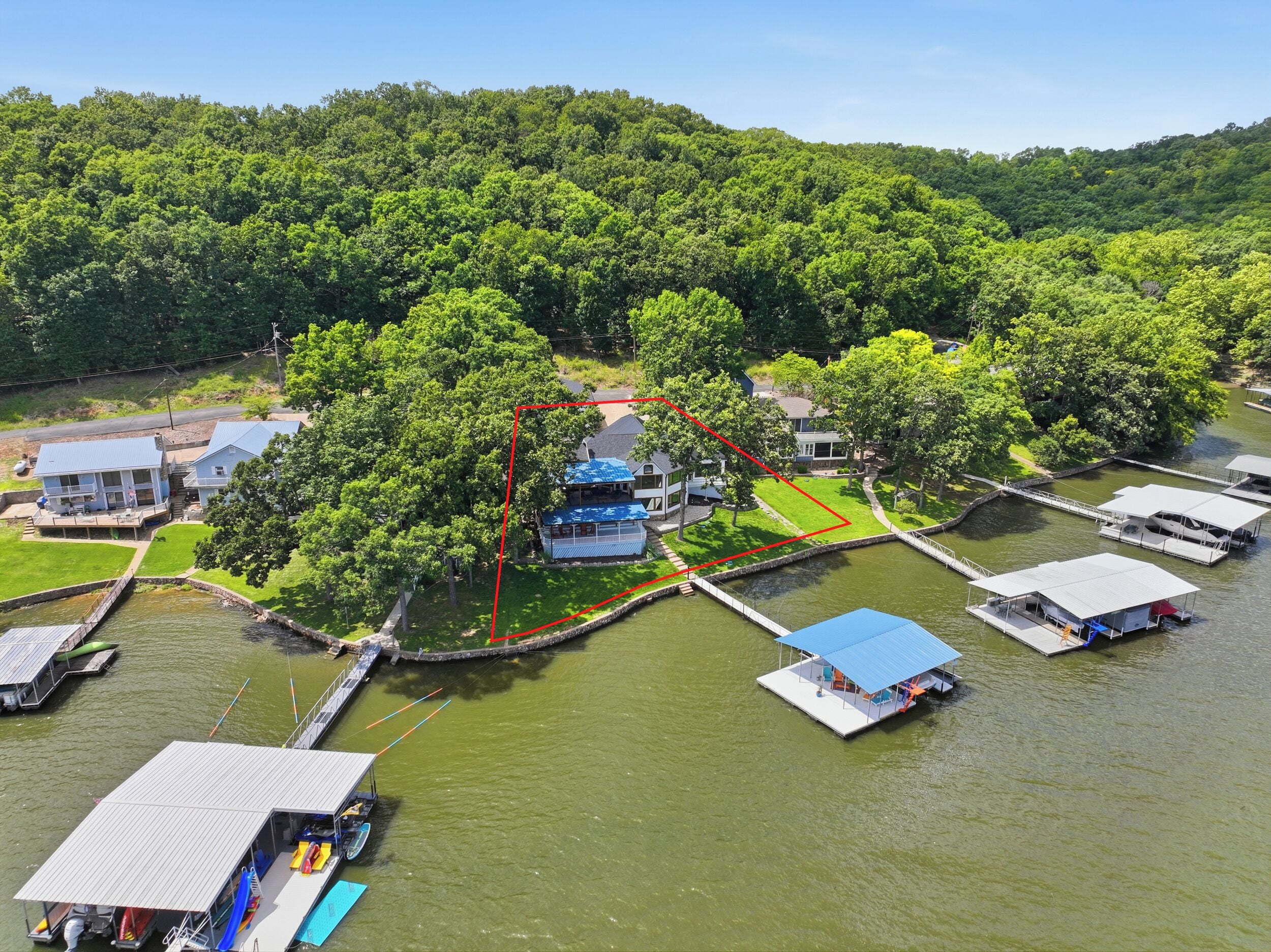 Uma propriedade à beira do rio, com barcos atracados, área gramada e uma casa com telhado azul.