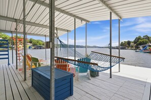 A covered outdoor area with a hammock, seating, and a view of a body of water. - A Stunning east facing, lake front home, in a cove, with Main Channel Views! (Sunrise Beach)