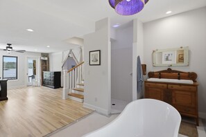 Un'ampia stanza con pavimento in legno, una vasca da bagno bianca, un comò in legno e una scala che conduce a un altro livello.