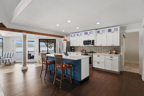 A modern kitchen with a central island, white cabinetry, and a view to the outside. - A Stunning east facing, lake front home, in a cove, with Main Channel Views! (Sunrise Beach)