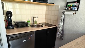 A compact kitchen with a sink, a dishwasher, and a countertop with a kettle and a coffee maker. - Studio cosy avec coin cabine – Le Sauze (Enchastrayes)