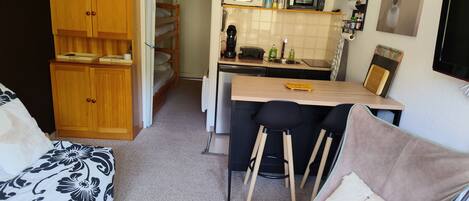 A compact living space with a kitchenette, a sofa, a dining table with chairs, and a wooden cabinet.