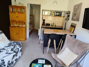 Ein kompakter Wohnraum mit Küchenzeile, einer Couch, einem Esstisch mit Stühlen und einem Holzschrank.