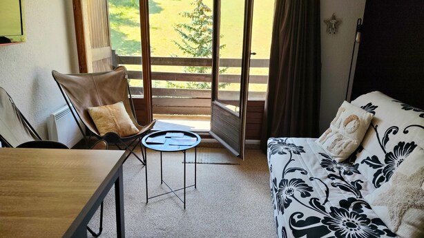 A room with a bed, a chair, a table, and a view of a grassy area through an open door. - Studio cosy avec coin cabine – Le Sauze (Enchastrayes)