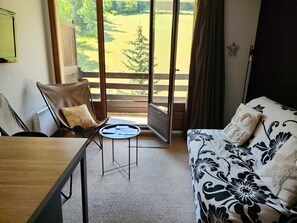 A room with a bed, a chair, a table, and a view of a grassy area through an open door. - Studio cosy avec coin cabine – Le Sauze (Enchastrayes)