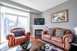 Ein Wohnzimmer mit Ledersofas, einem Flachbildfernseher, einem Kamin und einem großen Fenster.