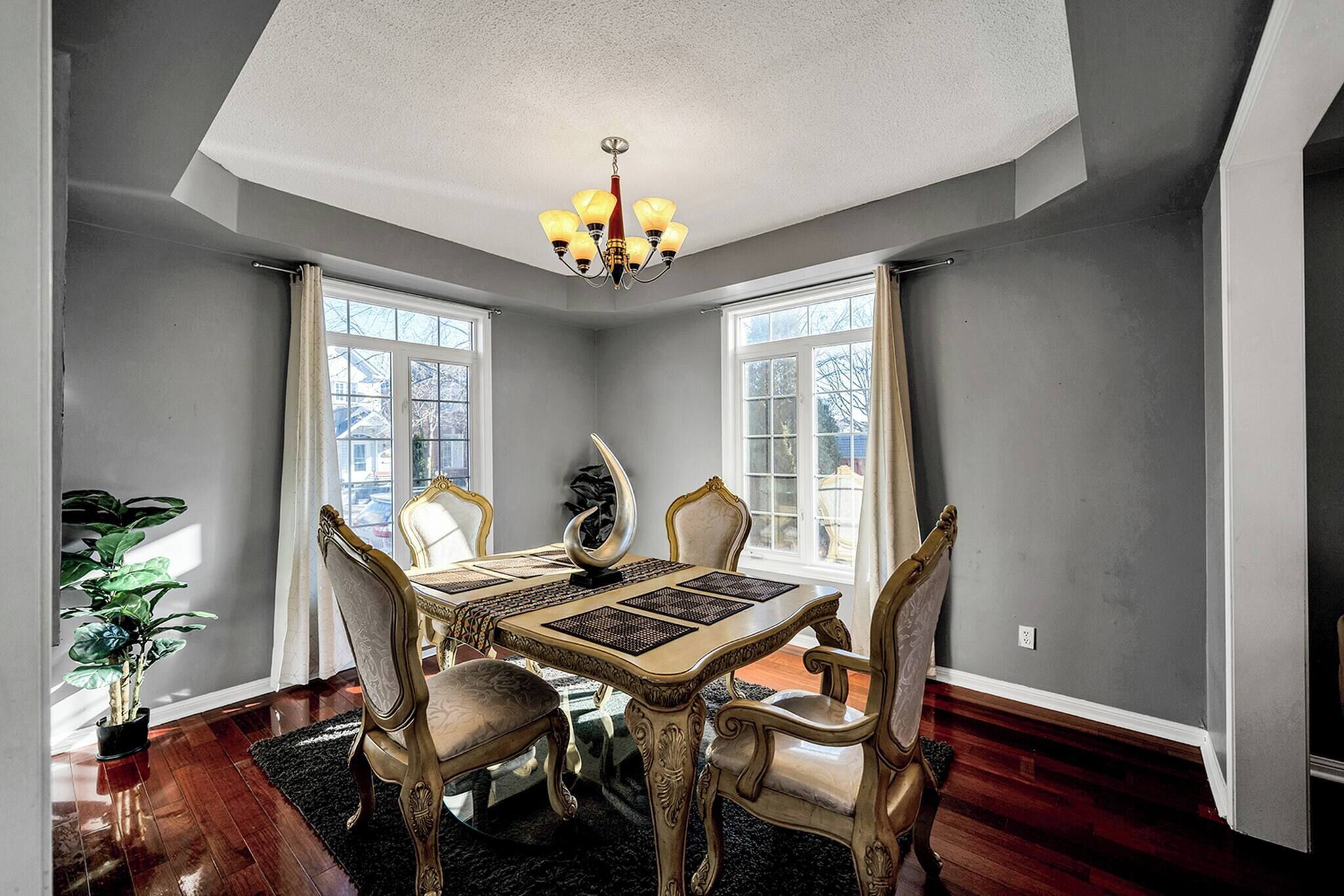 A dining room with a chandelier, a table with four chairs, and large windows.