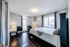 Ein Hotelzimmer mit einem großen Bett, zwei Nachttischlampen, einem Sessel, einem kleinen Tisch und Blick durch die Fenster hinaus.