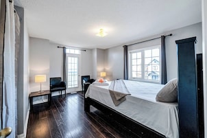 A hotel room with a large bed, two bedside lamps, a chair, a small table, and a view of the outside through the windows.