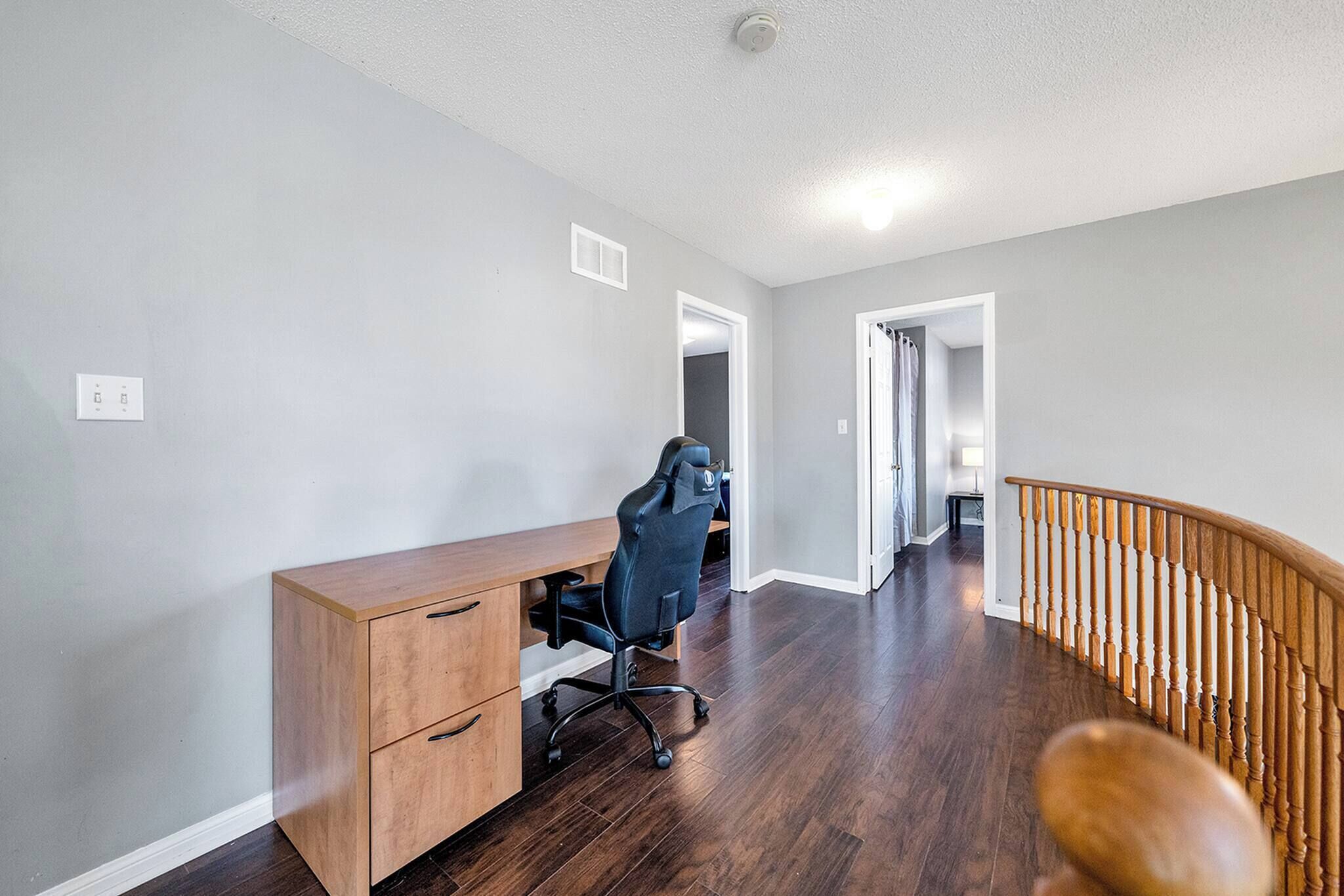 A room with a wooden desk, a black office chair, a wooden staircase, and a white ceiling.