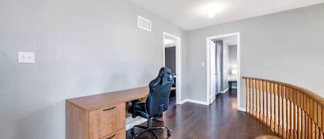 Een kamer met een houten bureau, een zwarte bureaustoel, een houten trap en een wit plafond.