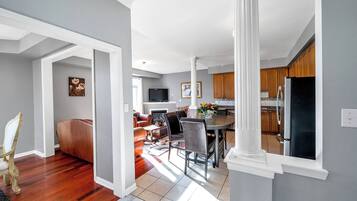 A spacious living room with a fireplace, a dining area with a table and chairs, and a kitchen with wooden cabinets and a refrigerator.