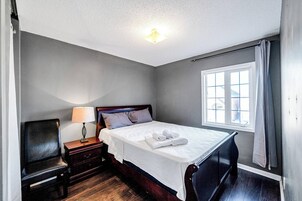 Una camera d'albergo con un letto, un comodino con una lampada, una sedia e una finestra con tende.