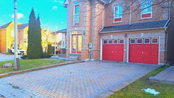 Um edifício residencial com calçada pavimentada, duas portas de garagem vermelhas e fachada de tijolos.