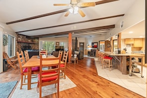 A spacious dining area with a wooden table and chairs, a ceiling fan, and a stone fireplace. - The Blue Spruce Log Cabin | Cozy 3BR | Munds Park (Munds Park)