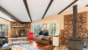 Una sala de estar acogedora con chimenea de piedra, un televisor y un ventanal grande.