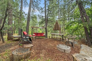 An outdoor seating area with a swing, picnic table, and benches. - The Blue Spruce Log Cabin | Cozy 3BR | Munds Park (Munds Park)