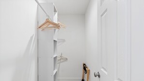 Ein schmaler Flur mit einer weißen Tür rechts, Holzboden und einer weißen Wand mit hängendem Holzbügel.