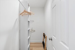 A narrow hallway with a white door on the right, a wooden floor, and a white wall with a hanging wooden hanger. - Spacious Coastal Getaway. Walk to Windansea beach, coffee shops, restaurants. (La Jolla)