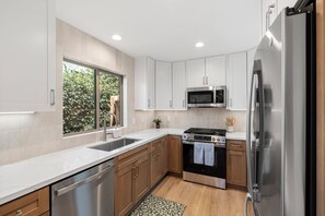 A modern kitchen with white cabinets, stainless steel appliances, and a window providing natural light. - Spacious Coastal Getaway. Walk to Windansea beach, coffee shops, restaurants. (La Jolla)