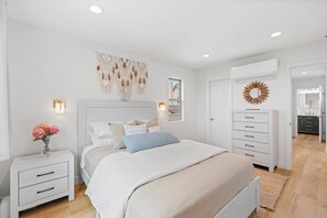 A bedroom with a bed, bedside tables, a dresser, and a wall-mounted macrame piece. - Spacious Coastal Getaway. Walk to Windansea beach, coffee shops, restaurants. (La Jolla)