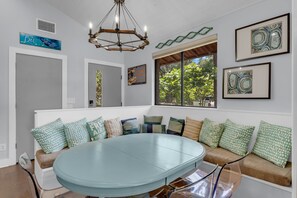 A room with a round table, a bench with cushions, a chandelier, and artwork on the walls.