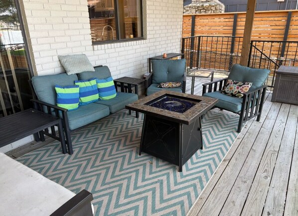 An outdoor patio with a sofa set, a fire pit, and a patterned rug.