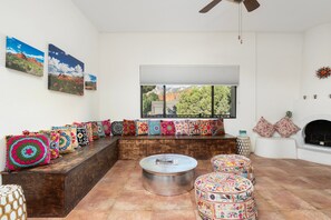 Una sala de estar con un sofá seccional, cojines coloridos, una mesa redonda y una chimenea.