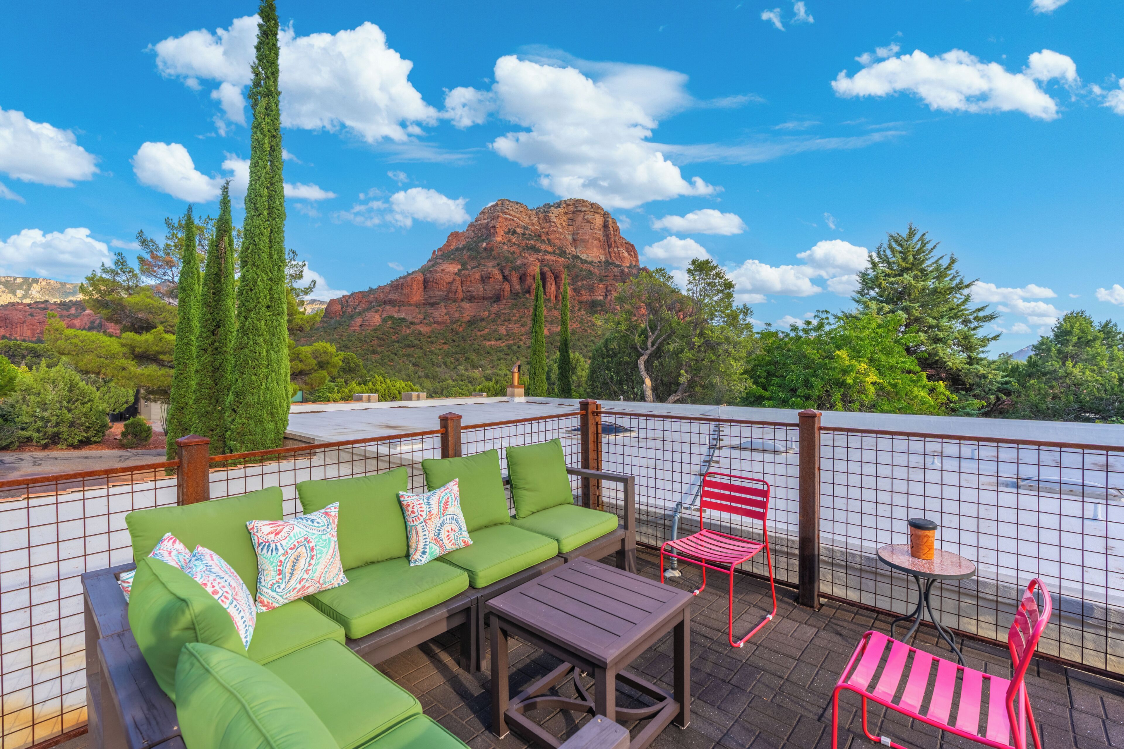 Eine Dachterrasse mit einem grünen Sofa, einem kleinen Tisch und zwei Stühlen mit Blick auf einen Berg und ein Gewässer.