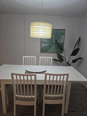 A dining area with a white table, two chairs, a pendant light, a framed picture, and a plant. - Spacious Dania Beach Condo Minutes from Beach, Airport & Cruise Port (Dania Beach)
