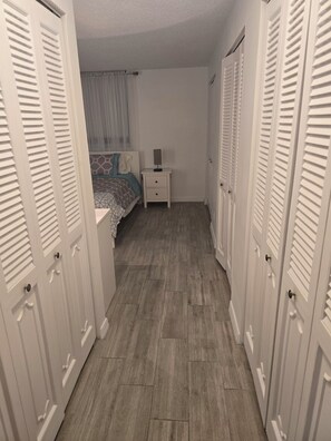 Un couloir étroit avec un lit, une table de chevet et des portes blanches.