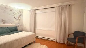 A bedroom with a bed, a chair, a fur rug, and a window with curtains.