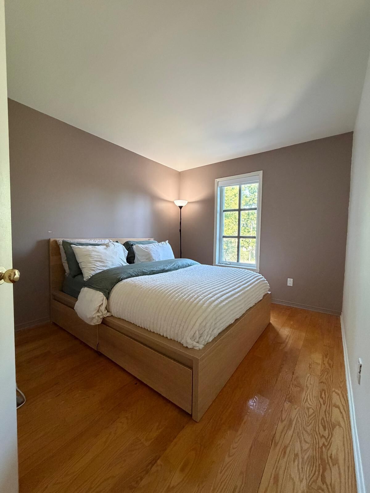 A bedroom with a bed, a window, and a floor lamp.