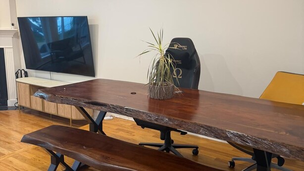 A conference table with a bench, a potted plant, and a television in the background.