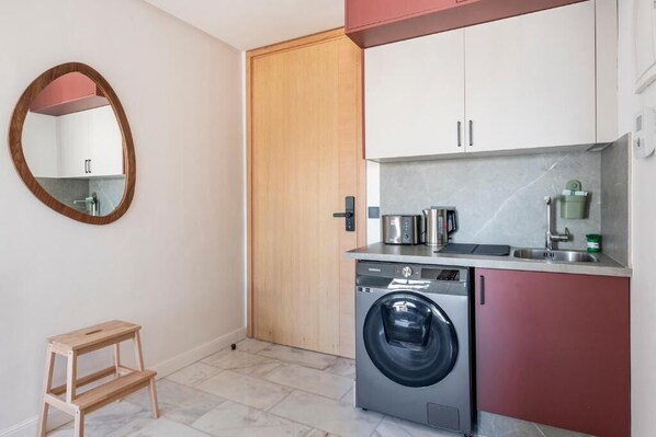 A compact kitchen with a washing machine, a small step stool, and a wooden door. - Charming Apartment 42 (Casablanca)