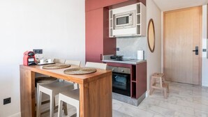 Cocina compacta equipada con microondas y horno, y una pequeña zona de comedor con una mesa y sillas de madera.