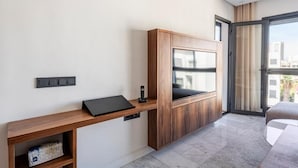 Una habitación moderna con un escritorio de madera, un televisor montado y un ventanal corredero que da a un balcón.