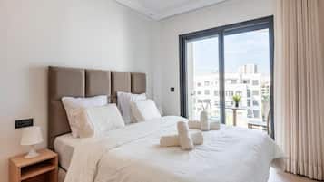 A hotel room with a large bed, a nightstand, and a view of the city through a large window.