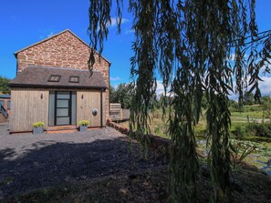 A stone building with a sloped roof, a wooden door, and a small garden area with plants. - The Old Mill (Telford)