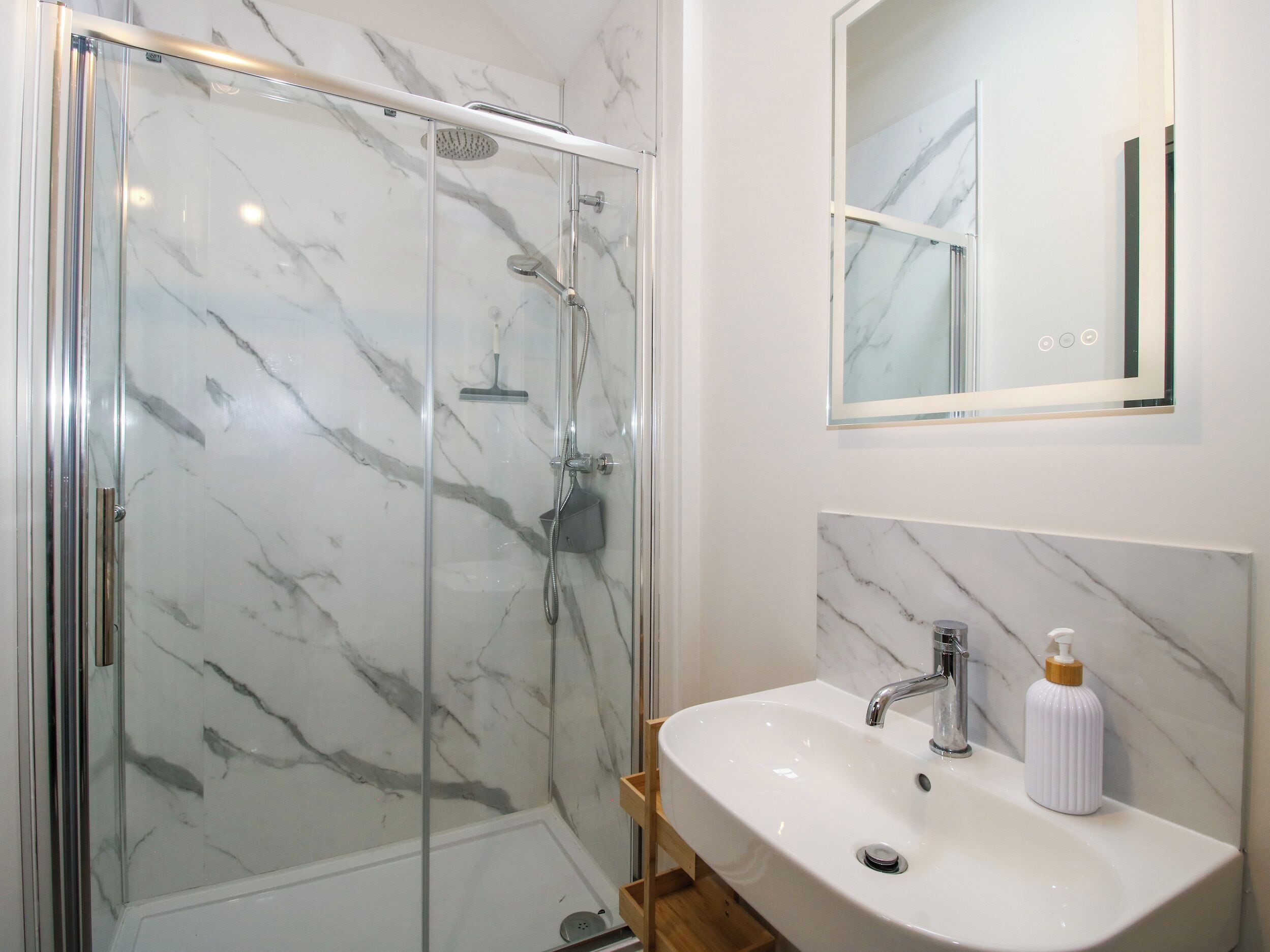 A bathroom with a glass-enclosed shower, a white sink with a modern faucet, and a marble backsplash.